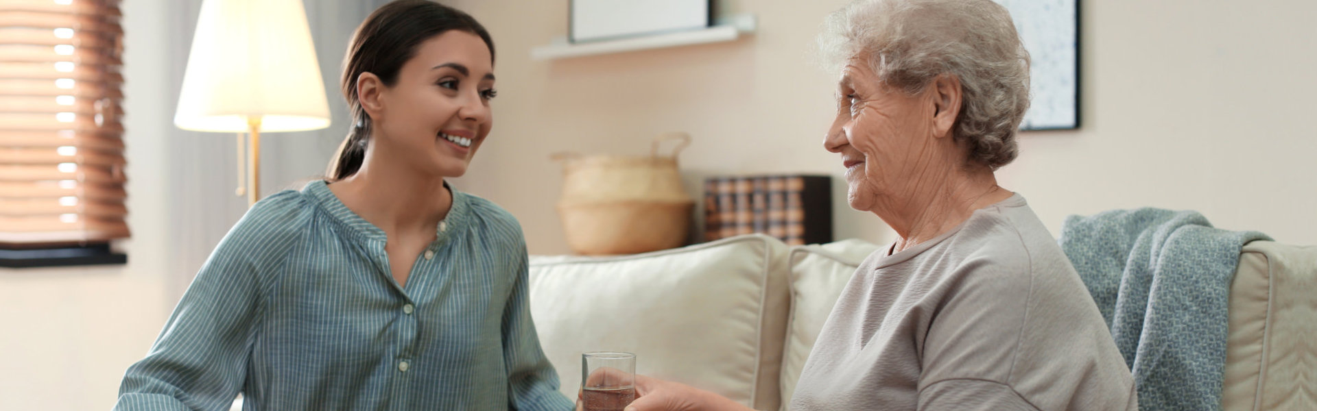 woman smiling at the senior woman while giving water